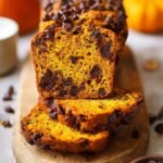 A golden loaf of Chocolate Chip Pumpkin Bread sliced on a wooden board with melted chocolate chips.