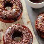 A tray of soft baked chocolate glazed donuts with shiny cocoa icing on a wire rack.