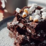 A stack of fudgy hot chocolate brownies topped with golden toasted mini marshmallows