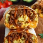 Four golden brown breakfast burritos stacked on a wooden board with sliced avocado and salsa