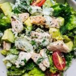 A bowl of creamy chicken salad with fresh green herbs and diced celery
