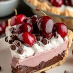 A slice of Chocolate Cherry Cream Pie showing layers of chocolate ganache, red cherry filling, and fluffy whipped cream.