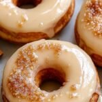 A stack of golden baked maple glazed donuts on a wire cooling rack with smooth maple glaze dripping down the sides.