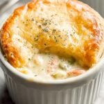 A golden brown Keto Chicken Pot Pie in a white ceramic dish with a slice removed to show the creamy chicken filling.