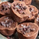A tray of smooth, dark chocolate cocoa fat bombs in mini liners on a marble surface.
