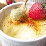 A bowl of smooth, yellow keto vanilla custard topped with a fresh mint leaf and a dusting of cinnamon.