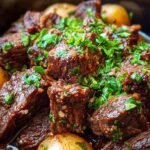 Cubed beef chuck roast in a slow cooker covered in garlic butter sauce and fresh parsley