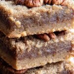 A stack of gooey Keto Pecan Pie Bars on a wooden serving board with scattered pecans