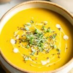 A bowl of creamy orange butternut squash soup garnished with pumpkin seeds and a swirl of cream