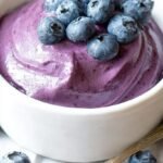 A bowl of creamy purple blueberry cream cheese spread next to a toasted bagel