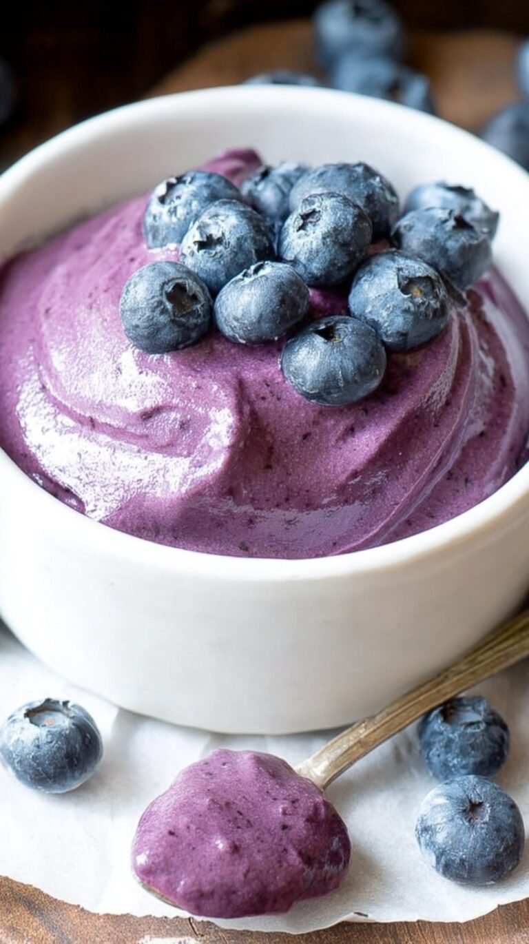 A bowl of creamy purple blueberry cream cheese spread next to a toasted bagel
