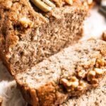 A golden-brown loaf of freshly baked coconut flour banana bread on a wooden board.