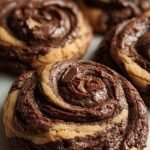 A stack of marbled brownie cookie swirls with golden edges and rich chocolate centers on a wire rack.