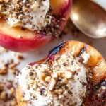 Grilled peach halves with a dollop of white mascarpone cream and fresh mint garnish