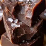 A stack of dense, dark keto chocolate fudge squares on a wooden board