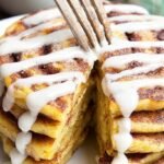 A stack of keto cinnamon roll pancakes with a white cream cheese glaze and cinnamon swirl