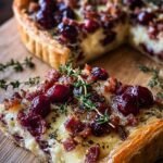 Golden brown mini cranberry brie tarts topped with crispy pancetta and fresh thyme on a serving tray.