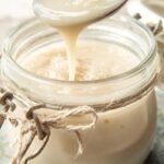 A glass jar filled with thick, creamy sugar free condensed milk on a wooden table.