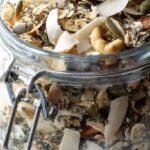 A glass jar filled with toasted keto muesli featuring almonds, pecans, and coconut flakes