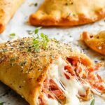 Two golden brown low carb keto calzones with melted cheese and pepperoni filling on a parchment-lined baking sheet.