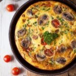 A golden brown Healthy English Breakfast Frittata in a cast iron skillet with tomatoes and turkey sausage.
