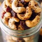 Golden roasted cashews mixed with crispy bacon bits on a parchment-lined baking sheet.