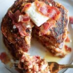 Golden brown paleo pancakes with shredded apples and crispy bacon bits on a white plate