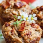 A stack of golden brown paleo apple muffins topped with crispy bacon bits on a wire cooling rack.