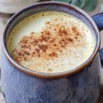A frothy healthy pumpkin spice latte in a ceramic mug with a sprinkle of spice on top.