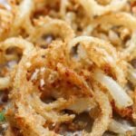Golden brown crispy fried onion straws on a white plate with paper towels.