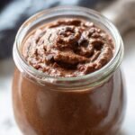 A bowl of silky smooth dark chocolate pudding topped with fresh berries and a sprig of mint.