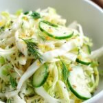 A bright bowl of shredded green cabbage, sliced cucumbers, and red onions tossed with fresh dill and vinegar dressing.