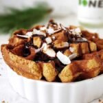 A golden brown protein waffle bread pudding in a square baking dish drizzled with maple syrup