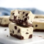 Square pieces of white cookies and cream fudge topped with crushed chocolate cookies on parchment paper