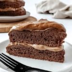 A slice of chocolate mocha protein cake topped with fluffy whipped dalgona coffee frosting on a white plate.
