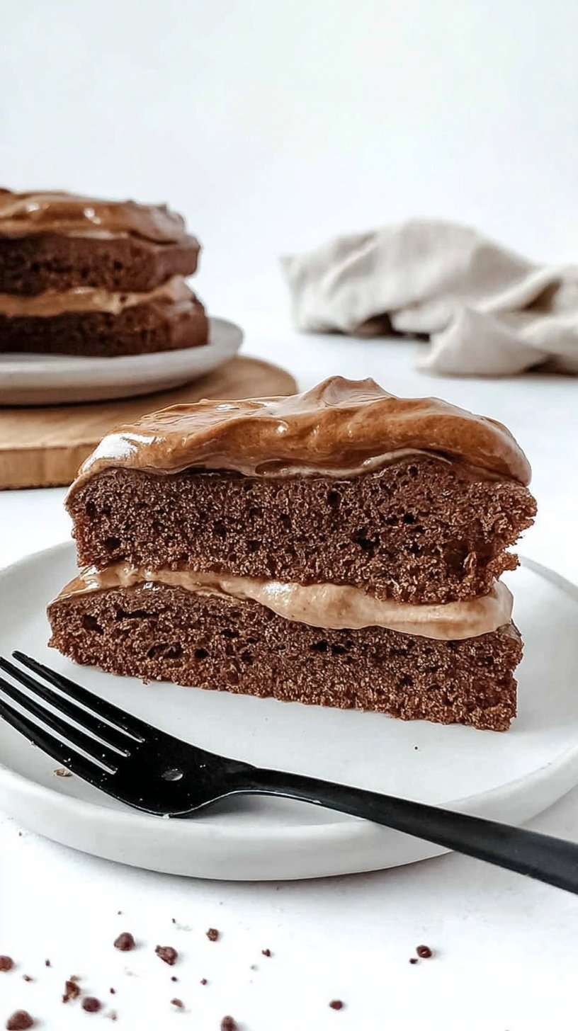 A slice of chocolate mocha protein cake topped with fluffy whipped dalgona coffee frosting on a white plate.