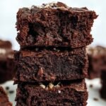 A stack of thick, fudgy chocolate protein brownies on a cooling rack.