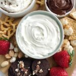 A bowl of creamy vanilla protein cheesecake dip served with fresh sliced strawberries and apple wedges.