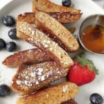 Golden brown protein french toast sticks stacked on a plate with fresh berries and syrup