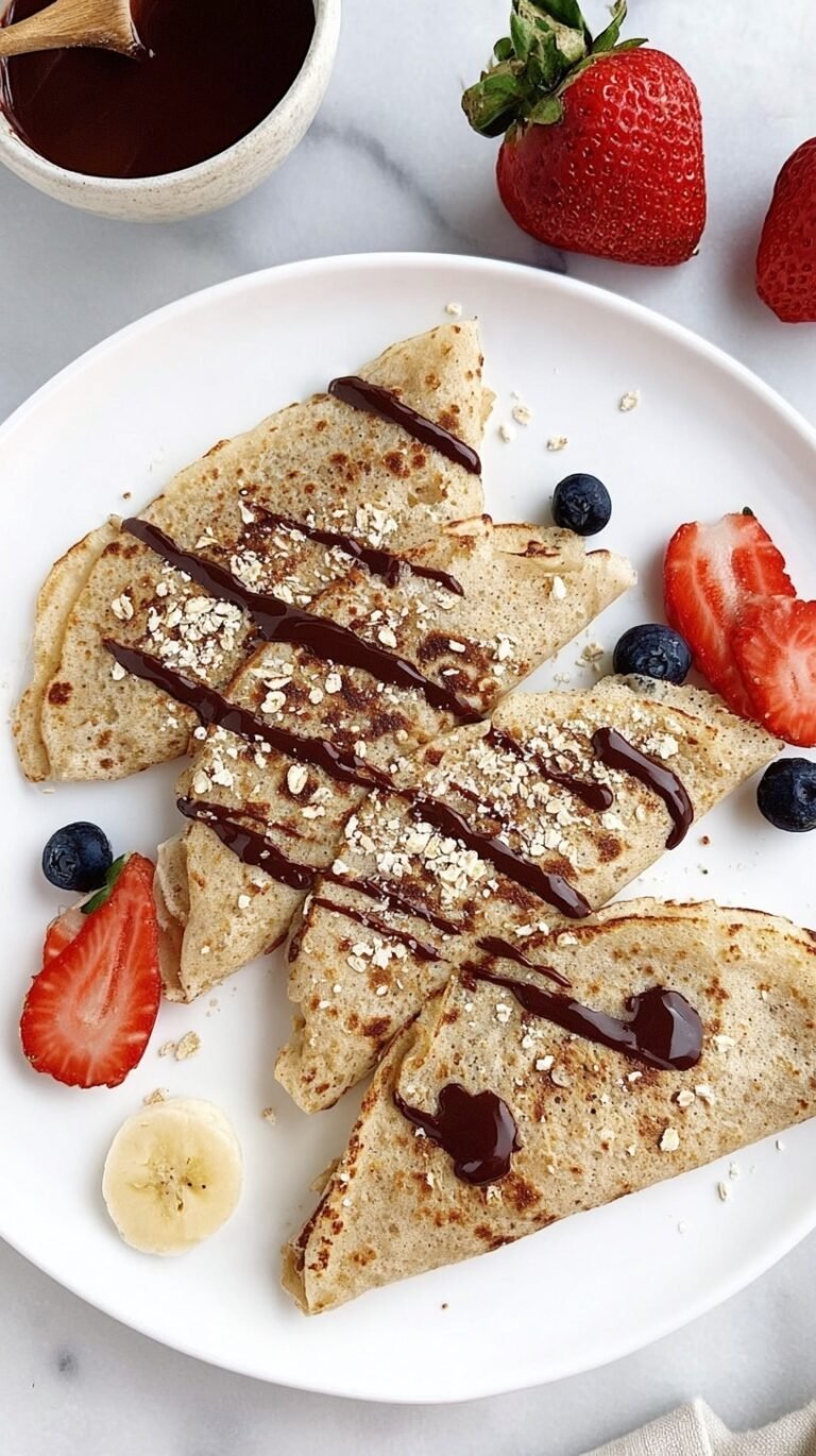 Thin golden oatmeal protein crepes folded on a white plate with fresh berries