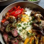 A bowl of thinly sliced ribeye steak with melted provolone cheese and sautéed peppers over cauliflower rice.