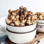 A large bowl of chocolate-coated popcorn topped with cookie crumbles and sea salt