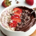 A glass jar filled with chocolate overnight oats topped with fresh diced strawberries and sugar-free chocolate chips.