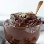 A bowl of thick chocolate edible brownie batter topped with sugar-free chocolate chips and a spoon.