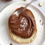 Creamy chocolate protein spread in a small white bowl with fresh strawberries nearby.