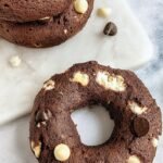 Four freshly baked chocolate whole wheat bagels on a baking sheet with mini chocolate chips