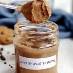 A glass jar of smooth, creamy homemade cookie butter next to apple slices and graham crackers.
