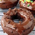 A plate of chocolate glazed donuts made in an air fryer on a wooden table.