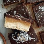Squares of smooth, creamy keto tahini fudge stacked on parchment paper.