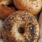 Four golden brown whole wheat bagels cooling on a wire rack in a bright kitchen.